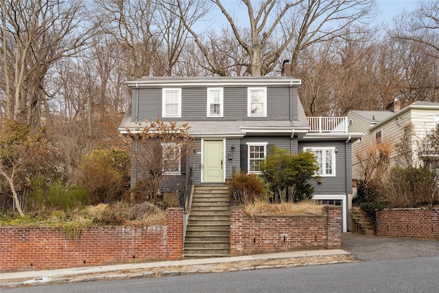 view of front facade with a balcony, driveway, a chimney, and roof with shingles