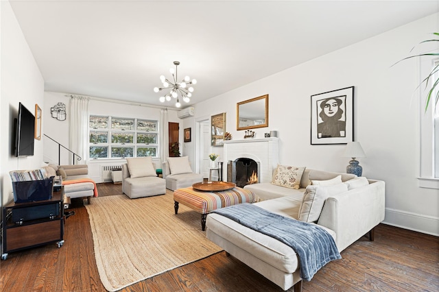 living area featuring a brick fireplace, radiator, a wall mounted air conditioner, wood finished floors, and a notable chandelier