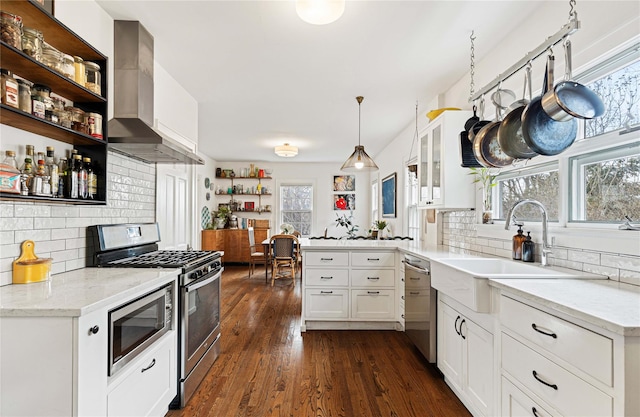 kitchen with dark wood-type flooring, a sink, appliances with stainless steel finishes, a peninsula, and wall chimney range hood