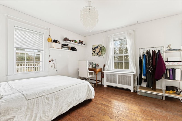 bedroom featuring an inviting chandelier, multiple windows, radiator, and wood finished floors