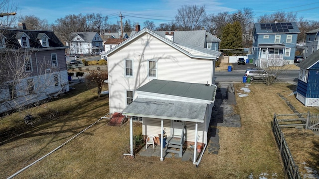 rear view of house with covered porch, fence, a yard, roof with shingles, and a residential view