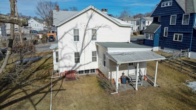 rear view of property with entry steps, roof with shingles, fence, and a lawn