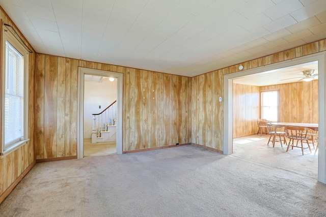 unfurnished room with carpet, wooden walls, and stairs