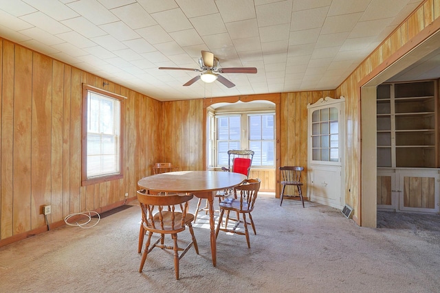 carpeted dining room with wood walls and ceiling fan