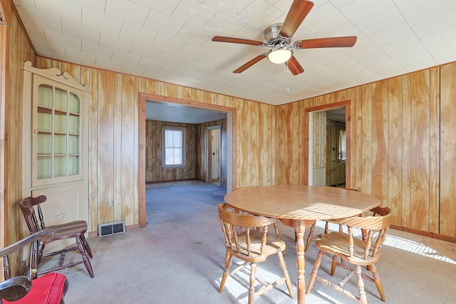 carpeted dining area featuring built in shelves, visible vents, wood walls, ceiling fan, and baseboards