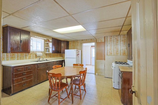 kitchen featuring white appliances, wallpapered walls, a drop ceiling, and light floors