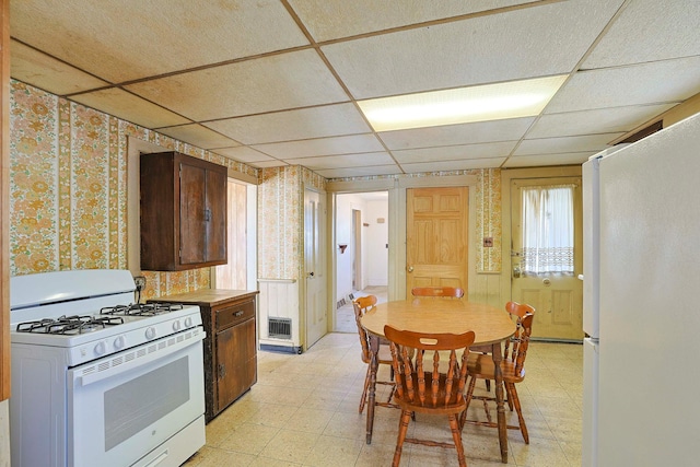 kitchen with white appliances, wallpapered walls, visible vents, a drop ceiling, and light floors