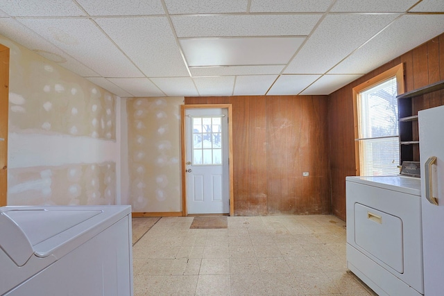 clothes washing area with laundry area, wood walls, washing machine and dryer, and light floors