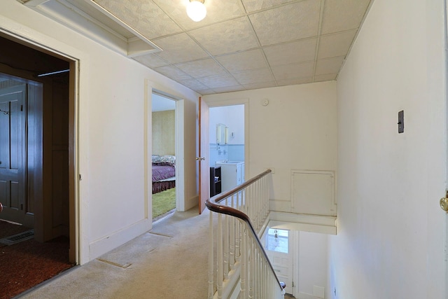 hallway featuring carpet floors, washer / clothes dryer, a drop ceiling, and an upstairs landing