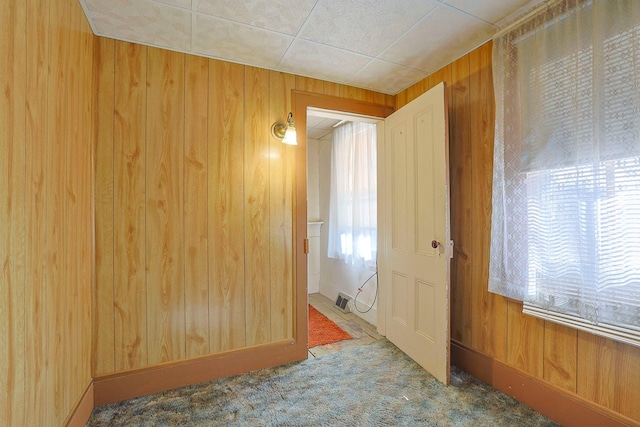 unfurnished room with carpet, visible vents, and wooden walls