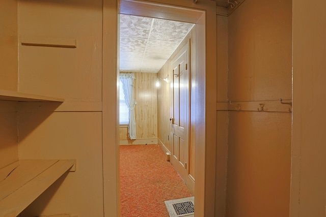 hallway with carpet, visible vents, and wooden walls