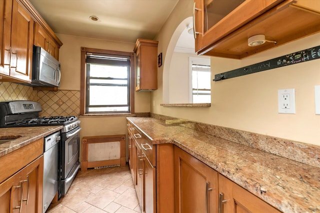 kitchen featuring stainless steel appliances, tasteful backsplash, brown cabinets, and light stone countertops