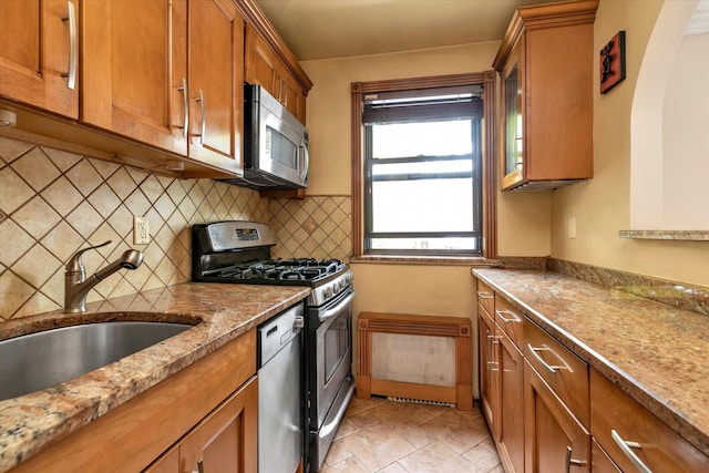 kitchen with stainless steel appliances, a sink, brown cabinets, tasteful backsplash, and glass insert cabinets