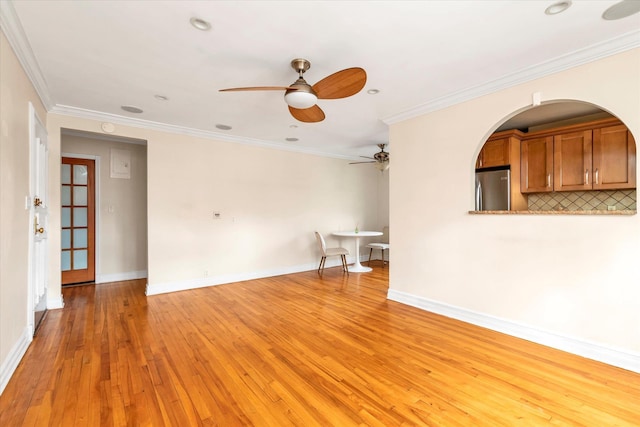 empty room with ceiling fan, ornamental molding, light wood-style flooring, and baseboards