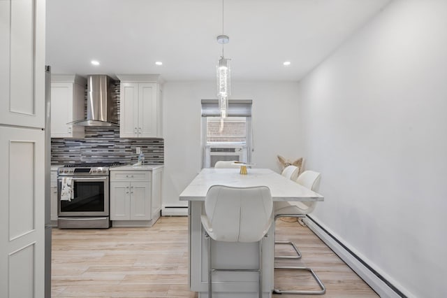 kitchen featuring a baseboard radiator, white cabinets, a kitchen breakfast bar, wall chimney range hood, and stainless steel range with gas stovetop