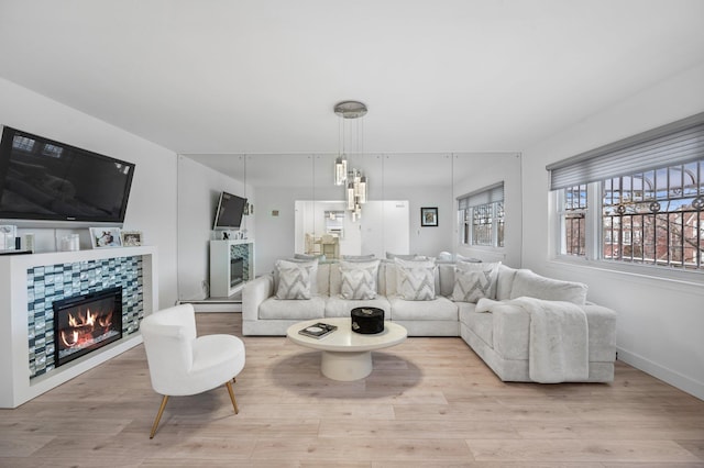 living room with a tiled fireplace, light wood-type flooring, and baseboards