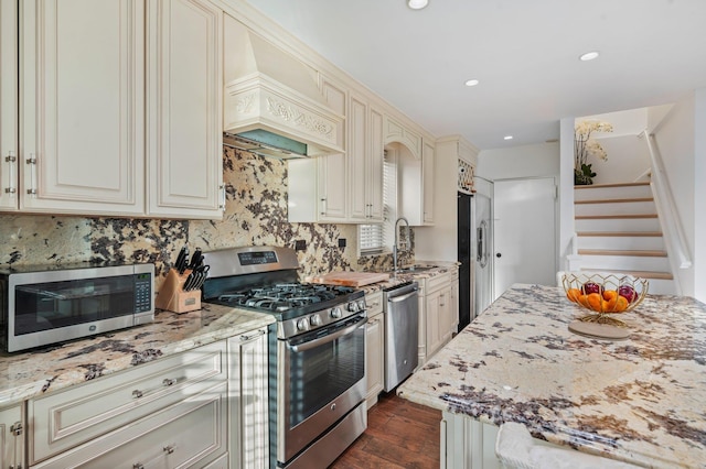 kitchen featuring premium range hood, appliances with stainless steel finishes, light stone counters, and cream cabinetry