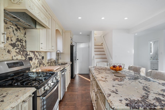 kitchen featuring cream cabinets, stainless steel appliances, custom exhaust hood, light stone countertops, and dark wood finished floors