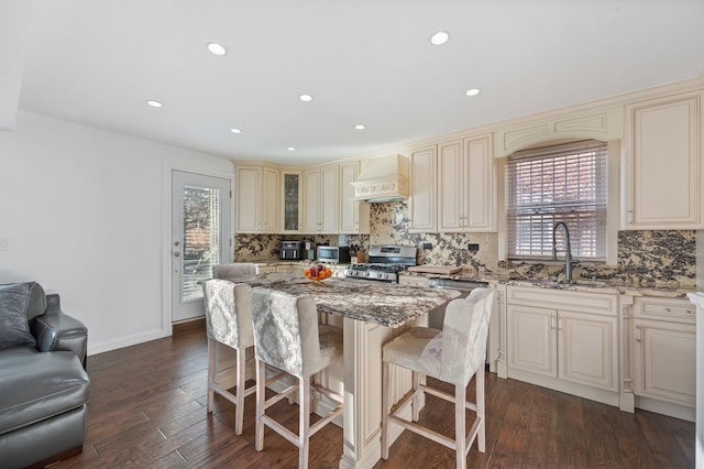 kitchen with a sink, a kitchen island, stainless steel range oven, cream cabinetry, and custom exhaust hood