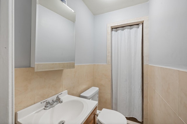 bathroom with toilet, a wainscoted wall, vanity, and tile walls