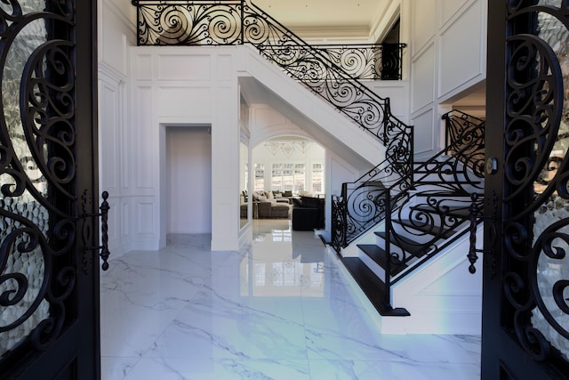 entryway featuring stairs, marble finish floor, ornamental molding, and a high ceiling