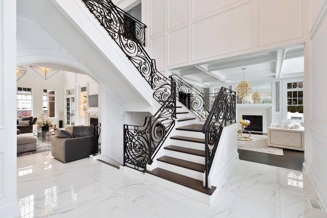 stairs featuring marble finish floor, a fireplace, a decorative wall, a towering ceiling, and an inviting chandelier