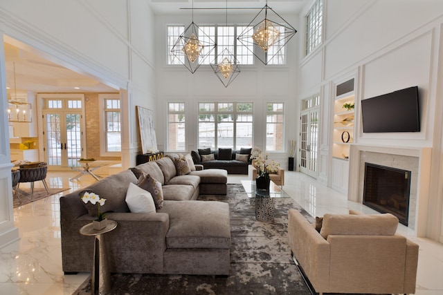 living area with an inviting chandelier, marble finish floor, french doors, a fireplace, and a decorative wall