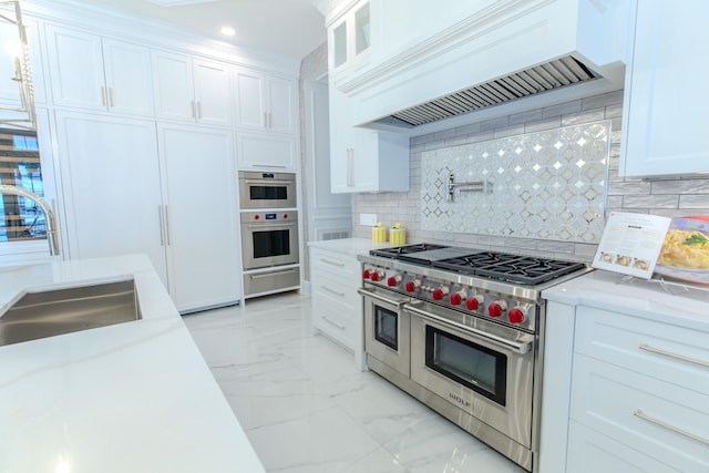 kitchen featuring marble finish floor, a warming drawer, stainless steel appliances, a sink, and premium range hood