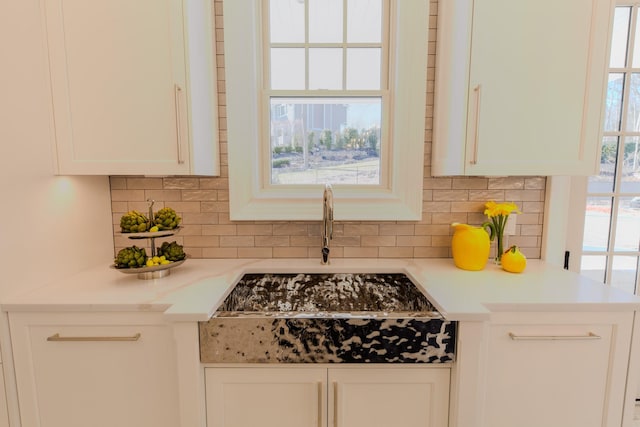 kitchen with light countertops, a sink, white cabinets, and decorative backsplash