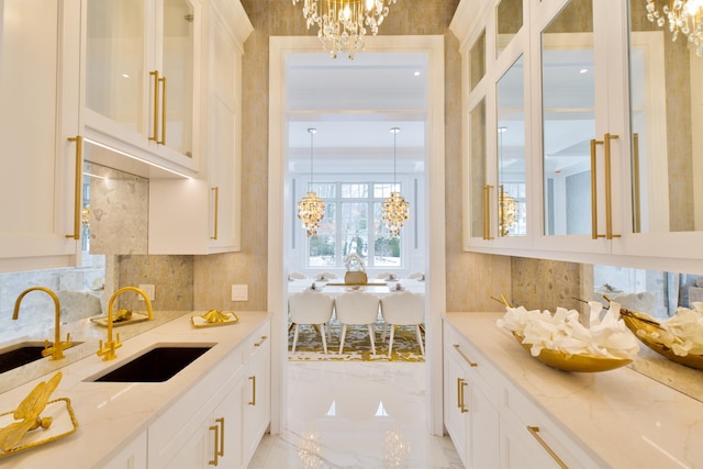 kitchen featuring light stone counters, a notable chandelier, a sink, marble finish floor, and pendant lighting