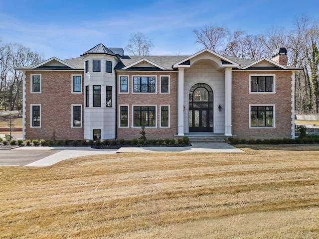 view of front of house with brick siding, a chimney, and a front yard