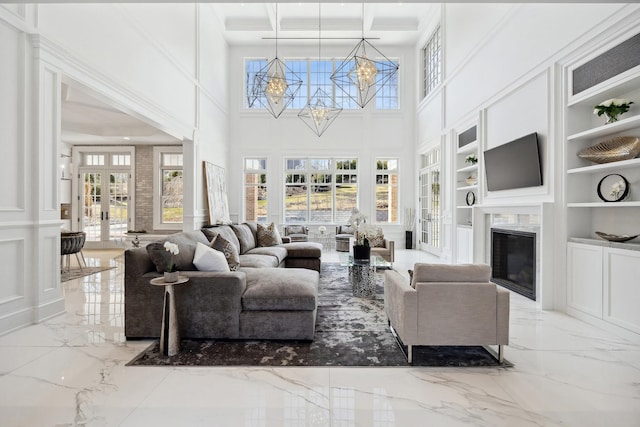 living room with a fireplace, a high ceiling, marble finish floor, french doors, and a notable chandelier