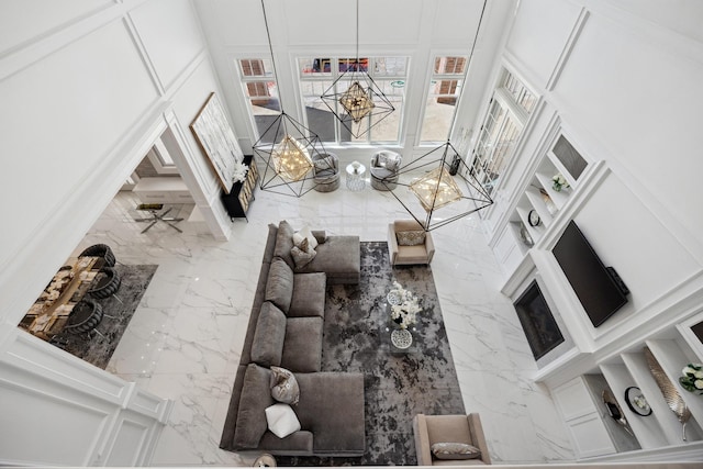 living room featuring an inviting chandelier, a decorative wall, marble finish floor, and a high ceiling