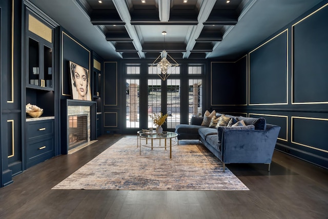 living area with a decorative wall, an inviting chandelier, beamed ceiling, dark wood-style flooring, and coffered ceiling