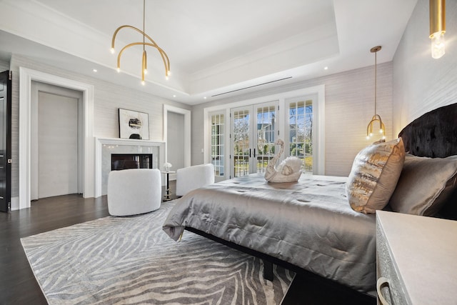 bedroom with french doors, access to exterior, a tray ceiling, a high end fireplace, and wood finished floors