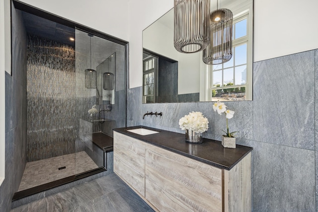 bathroom featuring marble finish floor, vanity, tile walls, and a tile shower
