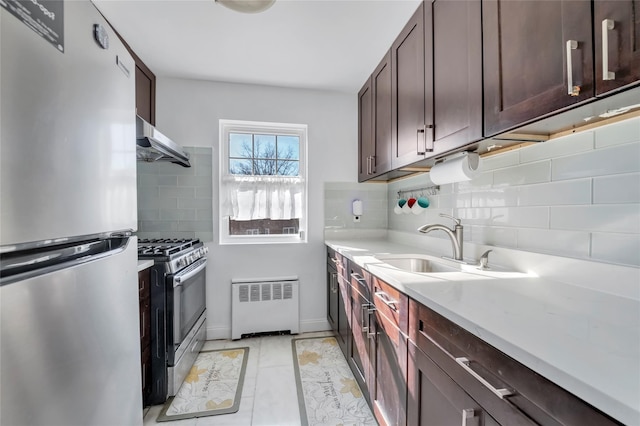 kitchen with under cabinet range hood, a sink, light countertops, appliances with stainless steel finishes, and radiator