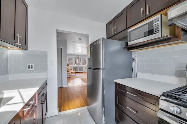 kitchen featuring dark brown cabinetry, decorative backsplash, stainless steel appliances, extractor fan, and light countertops