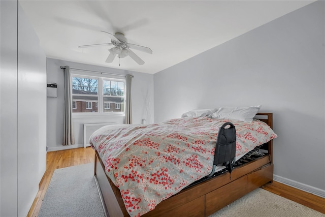 bedroom featuring a ceiling fan, radiator heating unit, light wood-style flooring, and baseboards