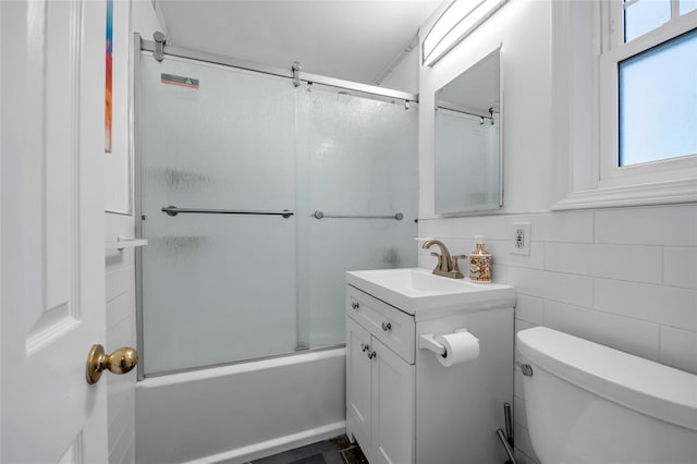 full bathroom with combined bath / shower with glass door, vanity, toilet, and tile walls