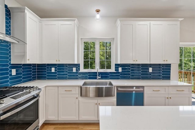 kitchen with white cabinets, wall chimney exhaust hood, appliances with stainless steel finishes, light countertops, and a sink