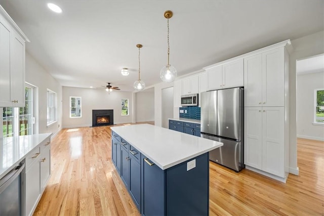 kitchen featuring open floor plan, stainless steel appliances, blue cabinetry, and light countertops