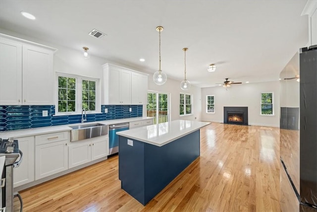 kitchen featuring hanging light fixtures, stainless steel appliances, light countertops, white cabinetry, and a sink