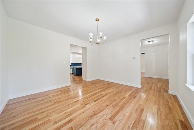 unfurnished room with light wood-type flooring, baseboards, and a notable chandelier