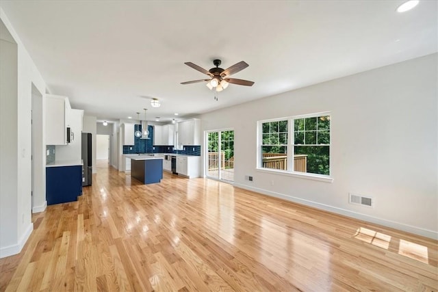 unfurnished living room with light wood-type flooring, visible vents, ceiling fan, and baseboards