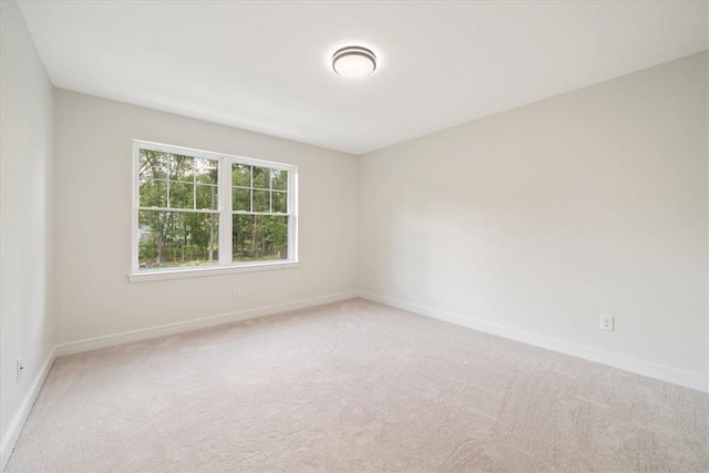 spare room featuring light carpet and baseboards