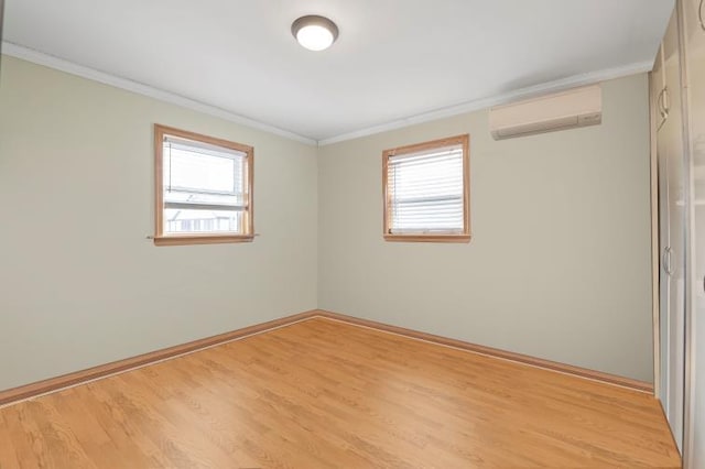 spare room featuring a wall unit AC, light wood finished floors, plenty of natural light, and crown molding