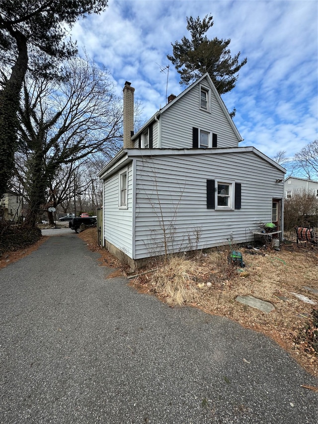 view of side of home with driveway and a chimney