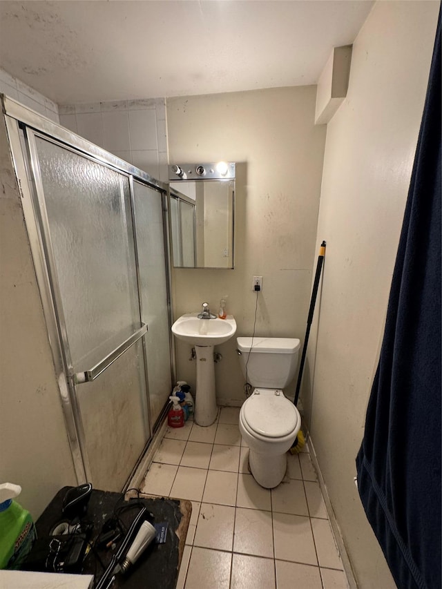 bathroom featuring toilet, a stall shower, tile patterned flooring, and a sink