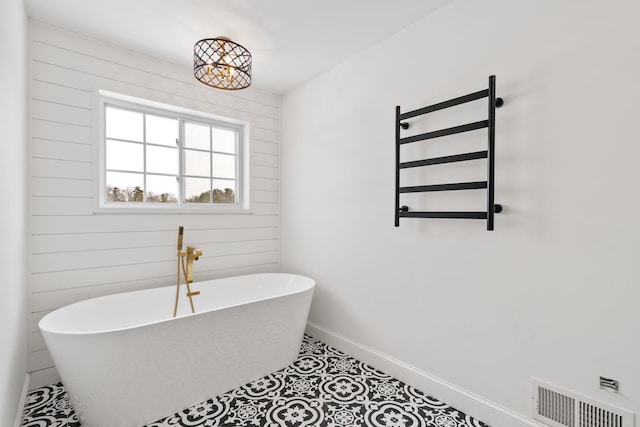 61 Surrey St, Rock Hill, NY 12775 - bathroom featuring a freestanding bath, a towel warmer, baseboards, tile patterned flooring, and wooden walls